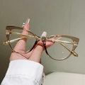 Detailansicht der Cat-Eye-Brille mit herzförmigem Strassstein auf dem Nasensteg - Champagner-Rahmen mit klarer Linse und Goldteilen