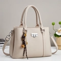Close-up of beige lychee grain leather handbag with silver twist lock and decorative charms - Apricot