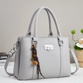 Close-up of light grey lychee leather handbag with silver lock and decorative charm - Gray
