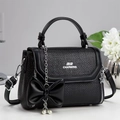 Detalle de bolso negro trenzado con logo plateado y colgante decorativo de lazo y perlas - Negro