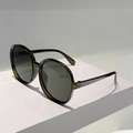 Detail view of round oversized sunglasses with olive translucent frames on a white pedestal - Transparent Green Frame Green Lens