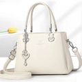 Close-up of beige fashion handbag featuring David Jones Paris logo and metal heart charm - Off-white