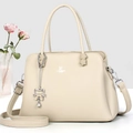 Detalle de bolso beige en cuero granulado con colgante de gato y correa ajustable - Albaricoque