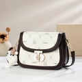 Chic cream saddle bag with brown trim, cartoon patterns and plush charm on marble background - Coffee and White