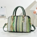 Green and white woven crossbody bag with pearl leaf charm and top handle on white surface - Green