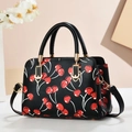 Close-up of black leather crossbody bag featuring red cherry prints and gold hardware - Black