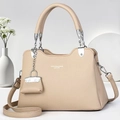 Detail of beige lychee leather handbag featuring silver hardware and a mini bag charm - Light Khaki