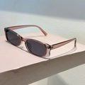 Close-up of translucent amber narrow frame sunglasses with dark grey lenses in sunlight - Transparent Grey Pink Frame Grey Lens