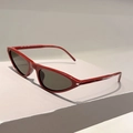 Detail der trendigen dunkelroten Cat-Eye-Sonnenbrille mit grauen Gläsern auf grauem Grund - Weinroter Rahmen Grüne Gläser