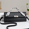 Detail of black pebbled leather handbag with gold twist lock and polka dot silk scarf handle - Black