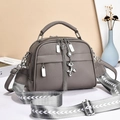 Detail of grey lychee textured crossbody bag with broad woven strap and silver puppy charm - Gray