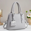 Gros plan d'un sac cabas gris clair grainé avec poignées rondes et petit charme - Gris