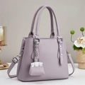 Sac à main violet élégant en cuir avec poignée et breloque décorative sur table blanche - Violet