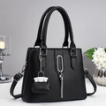 Elegant black lychee leather handbag with silver tassel and mini charm on a white desk - Black