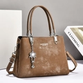 Detailed macro shot of vintage brown leather handbag with silver floral charm and metal buckle - Dark Khaki
