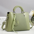 Detail of light green crossbody bag with woven handle and tennis pendant on white surface - Green