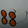 Retro round black sunglasses with orange lenses and golden metal temples on reflective surface - Black Frame Orange Lens
