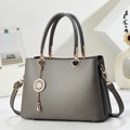 Grey pebbled leather handbag with gold hardware and charm in a minimalist studio setting - Gray