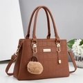 Détail d'un sac à main marron motif crocodile avec plaque dorée et pompon en peluche - Jaune Terre
