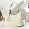 Elegante bolso beige con asas plateadas y colgante de camelia en un entorno minimalista - Blanco