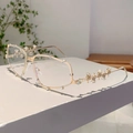 Detail der Y2K Sonnenbrille mit Goldrahmen und Strasssteinen auf weißem Sockel - Transparentes Glas Goldener Bügel