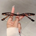 Lunettes œil-de-chat rétro en écaille et métal doré tenues sur un sol gris texturé - Monture Écaille Verres Transparents