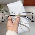 Detail of cat-eye glasses with gold and black metal frames held next to a white case - Black Gold Frame Transparent Lens