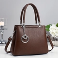 Détail du sac à main en cuir grainé marron foncé avec breloque argentée et bandoulière - café