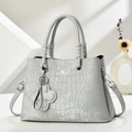 Detail of light grey crocodile pattern handbag with floral charm and silver hardware - Gray