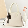 Elegante beige gewebte Schultertasche mit weißen Ledergriffen und dekorativem Anhänger - Cremeweiß