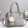 Close-up of color-block handbag with gold hardware and white plush doll pendant detail - Gray
