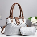 Detail view of silver snake-embossed handbag set with gold hardware and brown leather handles - Silver