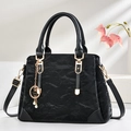 Elegant black pleated handbag with gold clover charm and pearl detail on a white podium - Pleated Texture (Style 1) / Black