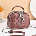 Pink V-quilted shoulder bag with silver chain strap and bear tassel charm on desk - Dusty Pink