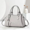 Grey pebbled leather crossbody bag with star charm and top handles in minimalist setting - Gray