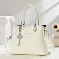 Detalle de bolso crema elegante con patrón de lichi y colgante de metal plateado - Blanco Roto