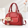 Detail van rode tas met lychee-textuur, gouden ringen en beige pluche wolkenhanger - Wijnrood
