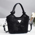 Schwarze Bucket Bag mit Knotengriff und silbernem Dreieck auf weißem Tisch präsentiert - Schwarz