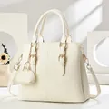 Elegant beige pebbled leather handbag with gold hardware and mini charm on white pedestal - Off-white