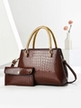 Detail of brown crocodile pattern handbag set with golden braided metal handles and wallet - Coffee