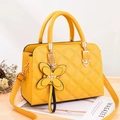 Yellow quilted leather handbag with floral charm and shoulder strap shown at 45 degrees - Turmeric