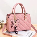 Pink quilted crossbody bag with gold hardware and a butterfly charm on a wooden surface - Pink
