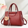 Close-up of burgundy lychee grain handbag with bear pendant and woven rope detail - Wine Red