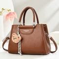 Close-up of brown litchi texture leather tote with fashion logo and teddy bear charm - Khaki/Earth Yellow