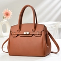 Tan lychee grain leather handbag with gold twist lock and shoulder strap on art pedestal - Earthy Yellow