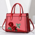 Red patent leather tote with 3D roses and adjustable strap in a minimalist setting - Red