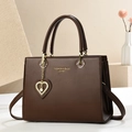 Brown leather handbag with gold heart pendant and pearl on white minimalist background - L25 H19 W12 / Coffee