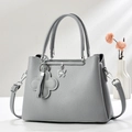 Grey textured leather tote bag with butterfly charm in a minimalist studio setting - Gray