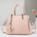 Detalle de bolso rosa claro con logo de marca y colgante floral en escritorio minimalista - Rosa