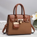 Detail of a brown woven tote with leather flap, gold padlock, and mini bag charm - Khaki/Earth Yellow